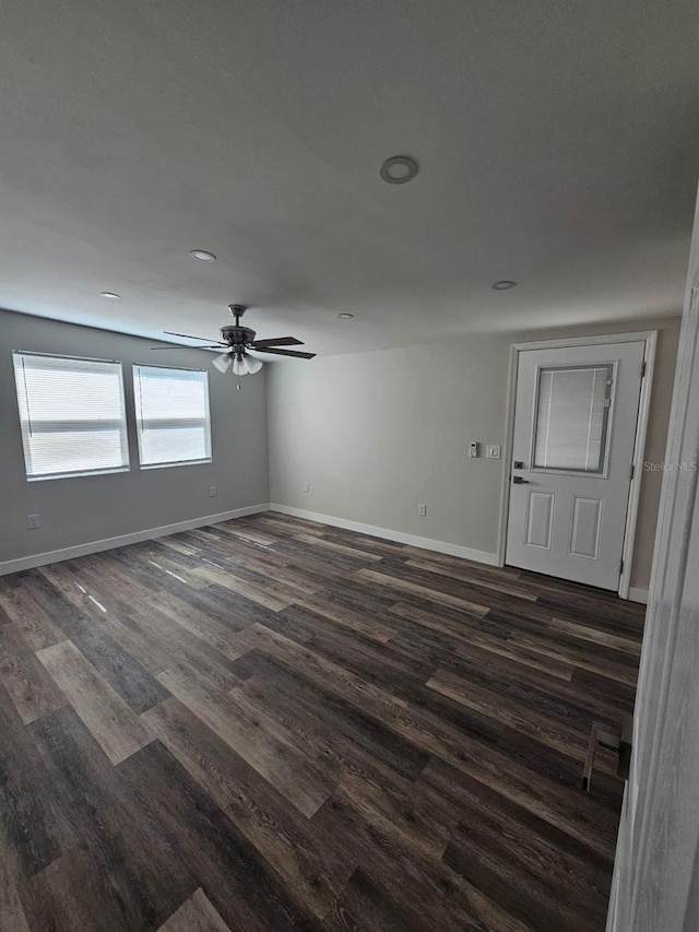 spare room with dark wood finished floors, a ceiling fan, and baseboards