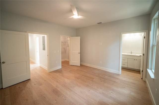 unfurnished bedroom with ceiling fan, connected bathroom, a spacious closet, a closet, and light wood-type flooring