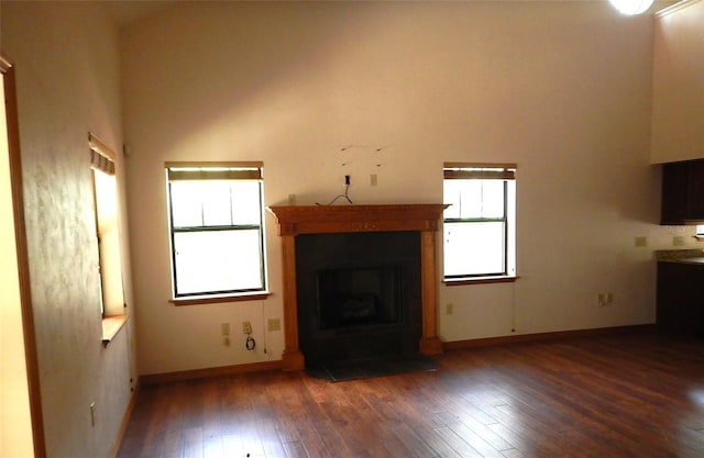 unfurnished living room featuring a towering ceiling, dark hardwood / wood-style flooring, and plenty of natural light