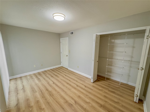 unfurnished bedroom with a textured ceiling, light wood-type flooring, and a closet