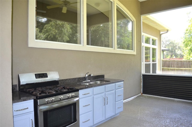 kitchen featuring dark stone counters, white cabinetry, ceiling fan, gas stove, and sink