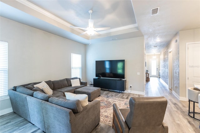 living room featuring light hardwood / wood-style floors, a raised ceiling, a wealth of natural light, and ceiling fan