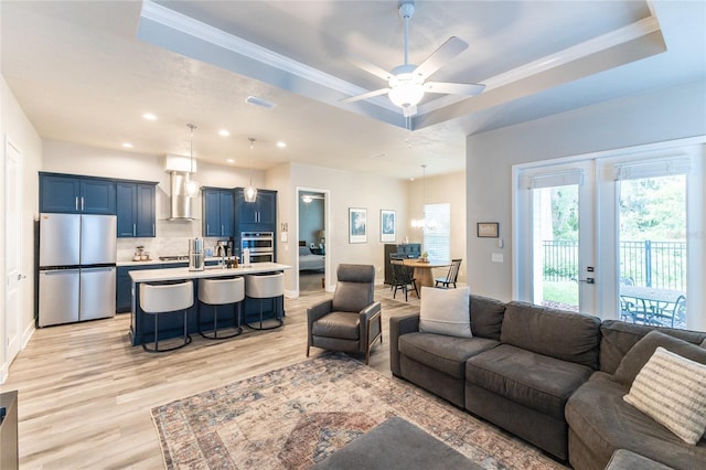 living room with light hardwood / wood-style flooring, a raised ceiling, ceiling fan, and ornamental molding