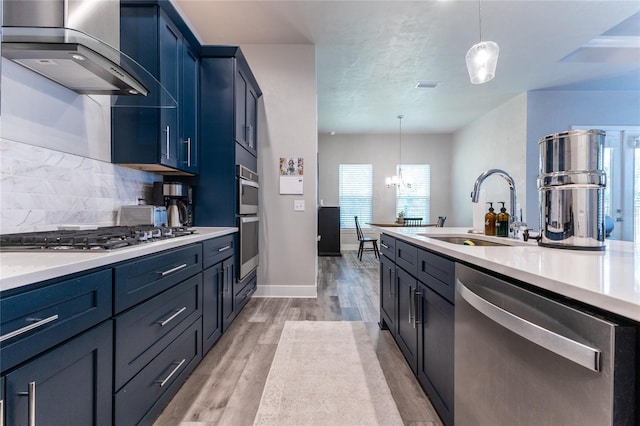 kitchen with backsplash, wall chimney exhaust hood, stainless steel appliances, sink, and pendant lighting