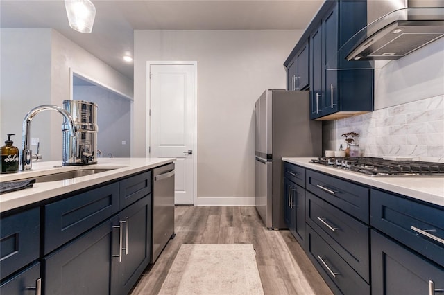 kitchen with blue cabinets, sink, range hood, light hardwood / wood-style floors, and stainless steel appliances