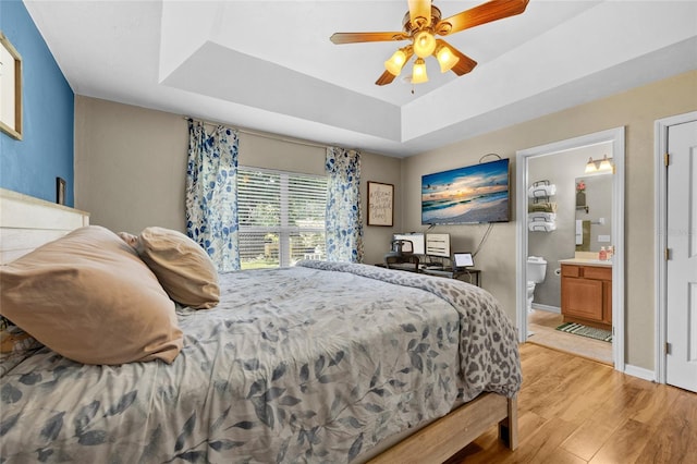 bedroom featuring ceiling fan, light hardwood / wood-style floors, connected bathroom, and a tray ceiling