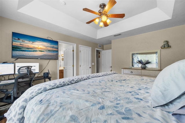 bedroom featuring a raised ceiling, ensuite bath, and ceiling fan