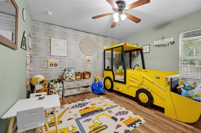 rec room with ceiling fan, wooden walls, and light hardwood / wood-style flooring