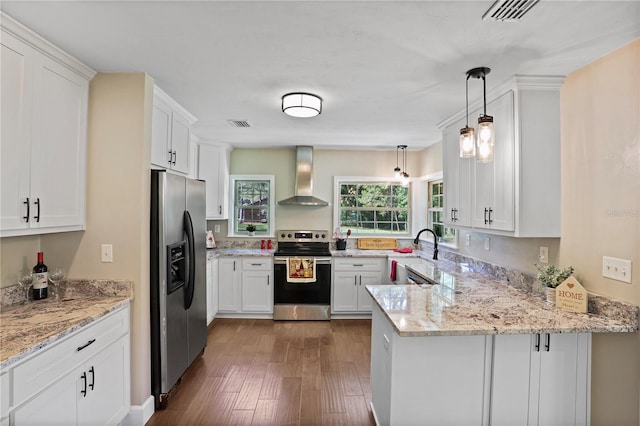 kitchen with appliances with stainless steel finishes, kitchen peninsula, white cabinets, wall chimney range hood, and decorative light fixtures