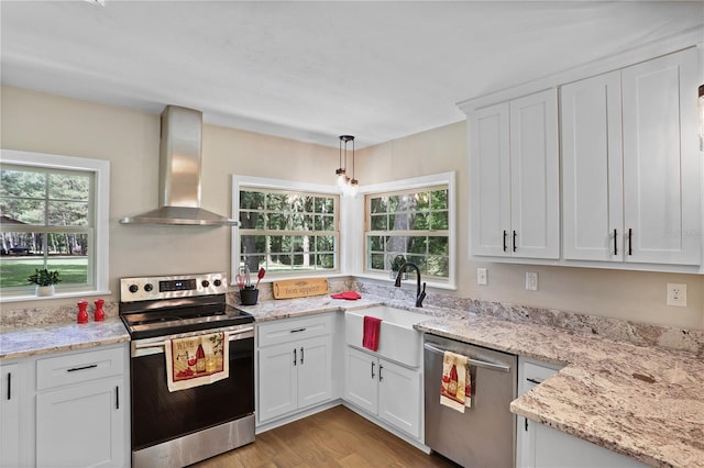 kitchen with stainless steel appliances, sink, white cabinets, wall chimney exhaust hood, and pendant lighting