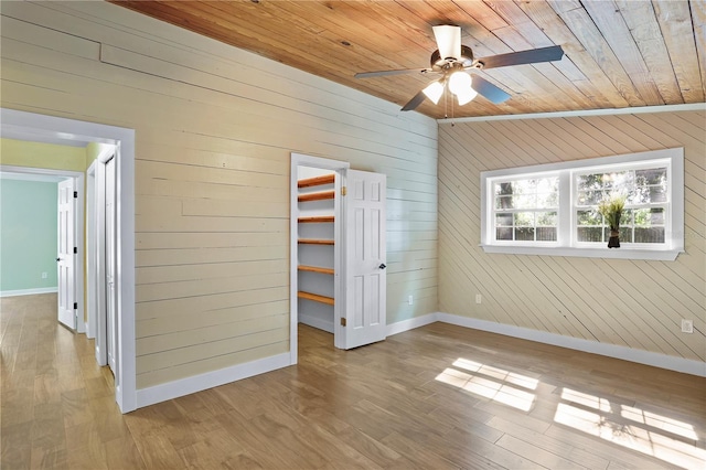 unfurnished bedroom featuring wooden ceiling, ceiling fan, a spacious closet, wooden walls, and light hardwood / wood-style flooring