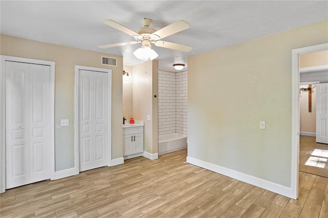 unfurnished bedroom with two closets, ceiling fan, light hardwood / wood-style floors, and ensuite bath