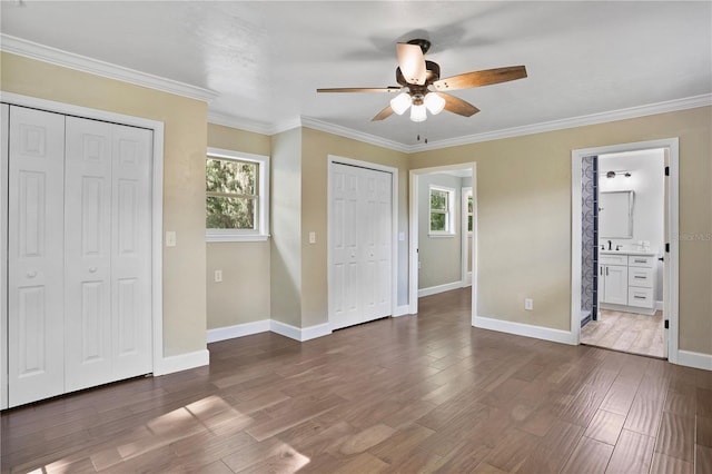 unfurnished bedroom with connected bathroom, wood-type flooring, ceiling fan, ornamental molding, and two closets