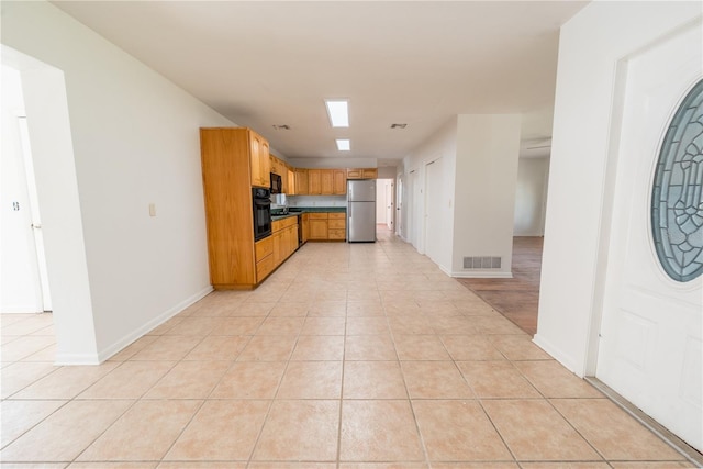 kitchen with light tile patterned floors, black oven, and stainless steel refrigerator