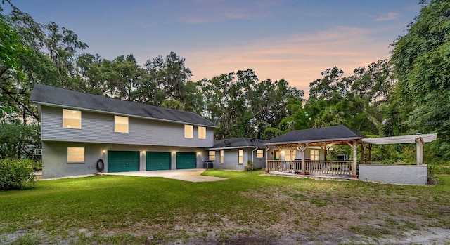 back house at dusk with a lawn, covered porch, central AC unit, and a garage