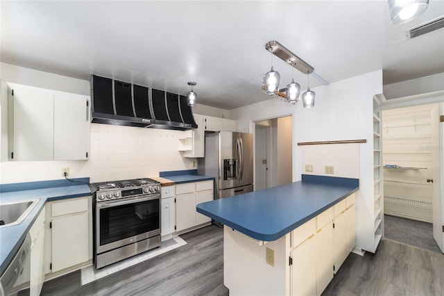 kitchen with wall chimney range hood, dark hardwood / wood-style flooring, kitchen peninsula, decorative backsplash, and appliances with stainless steel finishes