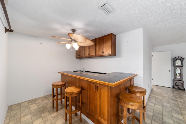 bar featuring a textured ceiling, tile counters, and ceiling fan