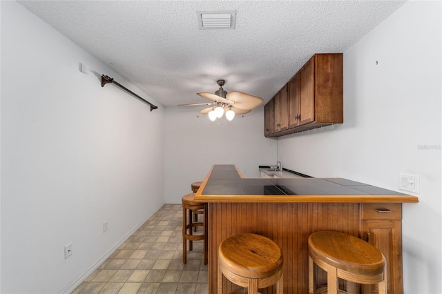 bar featuring tile counters, ceiling fan, sink, and a textured ceiling