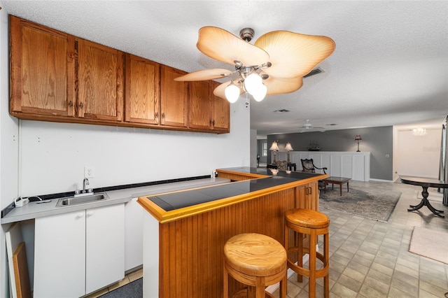 kitchen featuring a kitchen breakfast bar, ceiling fan, sink, and a textured ceiling