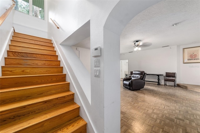 staircase with a textured ceiling, parquet floors, and ceiling fan