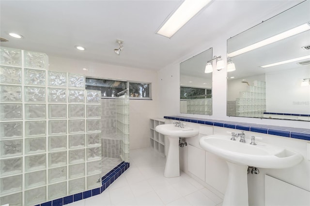 bathroom with a tile shower, tile patterned flooring, double sink, and tile walls