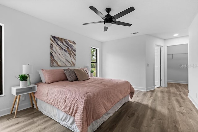 bedroom featuring a walk in closet, ceiling fan, and light hardwood / wood-style flooring