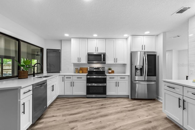 kitchen featuring white cabinetry, appliances with stainless steel finishes, sink, and light hardwood / wood-style flooring