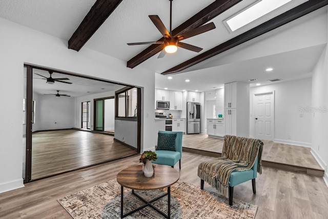 living room with ceiling fan, lofted ceiling with skylight, and light wood-type flooring