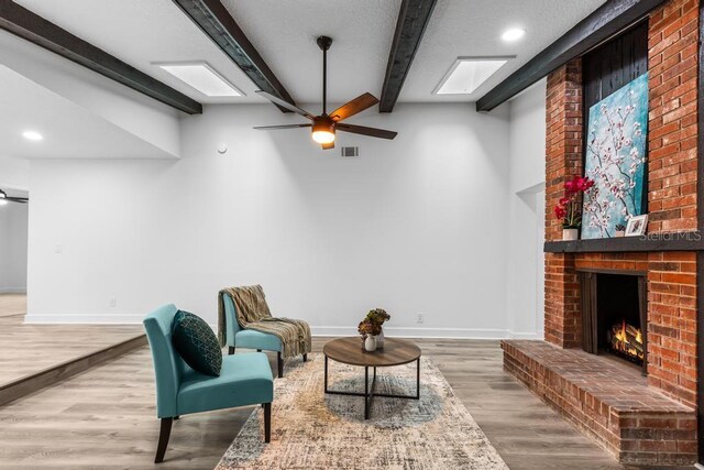 living area featuring a fireplace, beamed ceiling, hardwood / wood-style flooring, ceiling fan, and a textured ceiling