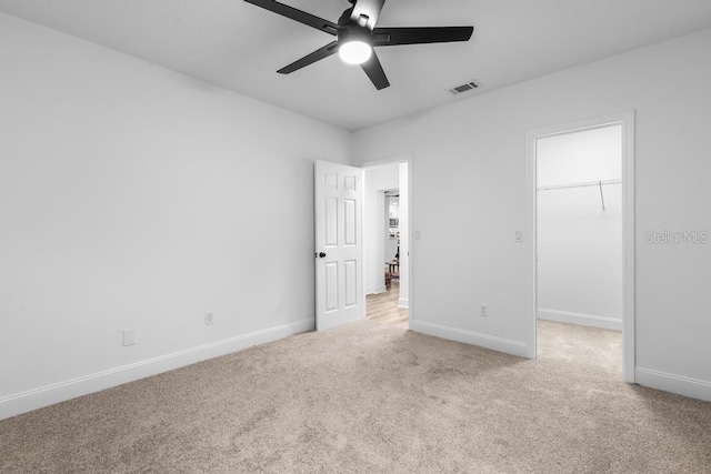 unfurnished bedroom with light carpet, a walk in closet, a closet, and ceiling fan