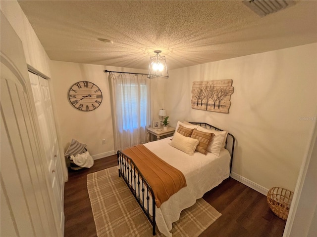 bedroom with dark hardwood / wood-style flooring, a textured ceiling, and a notable chandelier