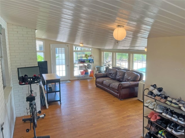 living room with vaulted ceiling, brick wall, a fireplace, and light hardwood / wood-style floors