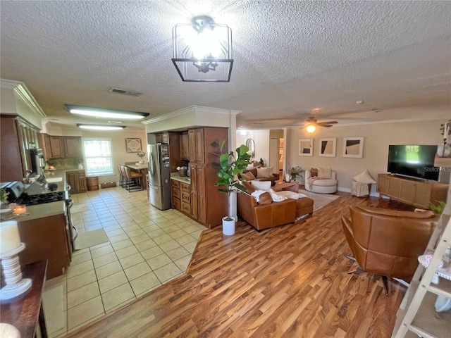 living room with ceiling fan, crown molding, light hardwood / wood-style flooring, and a textured ceiling