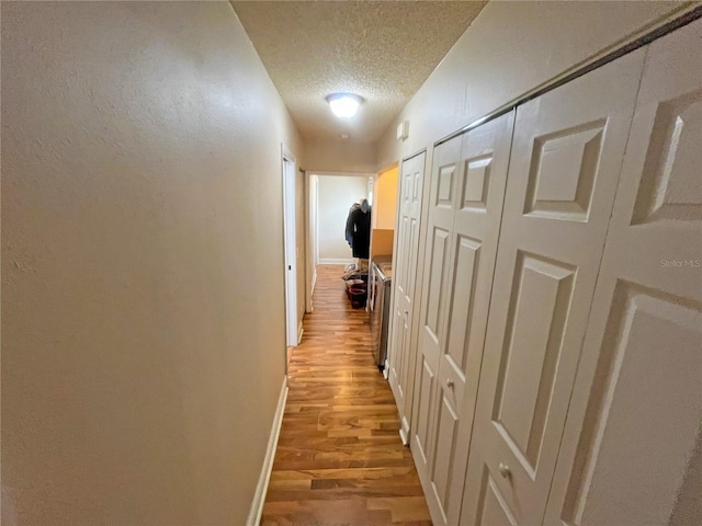 hall with light hardwood / wood-style floors and a textured ceiling