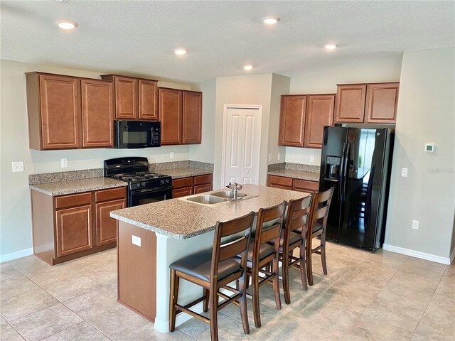 kitchen with black appliances, a center island with sink, sink, light tile patterned floors, and a kitchen breakfast bar