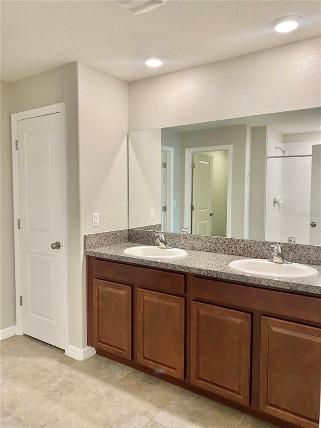 bathroom with tile patterned flooring, walk in shower, a textured ceiling, and dual bowl vanity