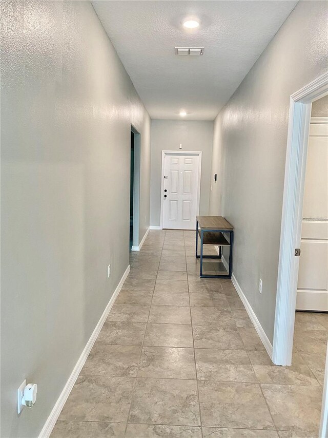 hall with a textured ceiling and light tile patterned floors