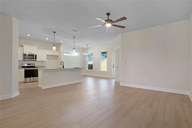 unfurnished living room featuring recessed lighting, light wood-style flooring, a sink, baseboards, and ceiling fan with notable chandelier