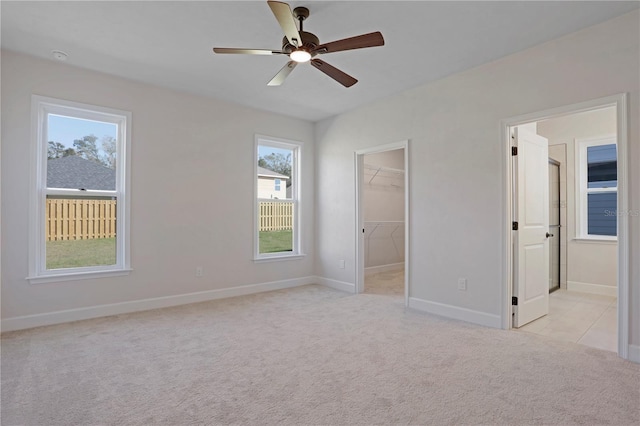 unfurnished bedroom featuring baseboards, light colored carpet, ensuite bathroom, a walk in closet, and a closet