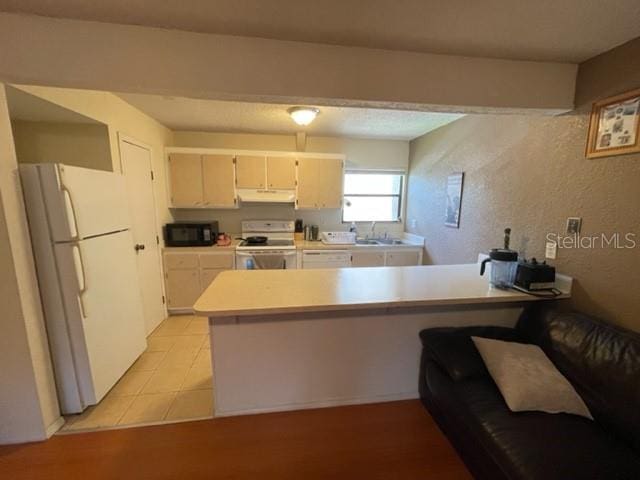 kitchen with light tile patterned flooring, white cabinets, white appliances, sink, and kitchen peninsula