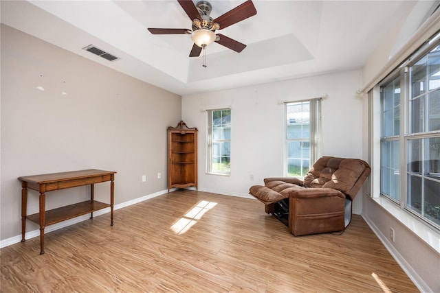 sitting room with ceiling fan, a tray ceiling, and light hardwood / wood-style flooring