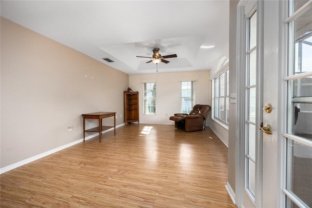 unfurnished room featuring a raised ceiling, ceiling fan, and light wood-type flooring