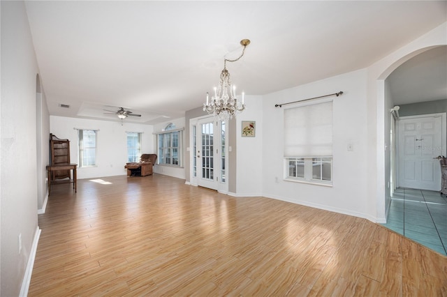 unfurnished living room featuring ceiling fan with notable chandelier, light hardwood / wood-style flooring, and plenty of natural light