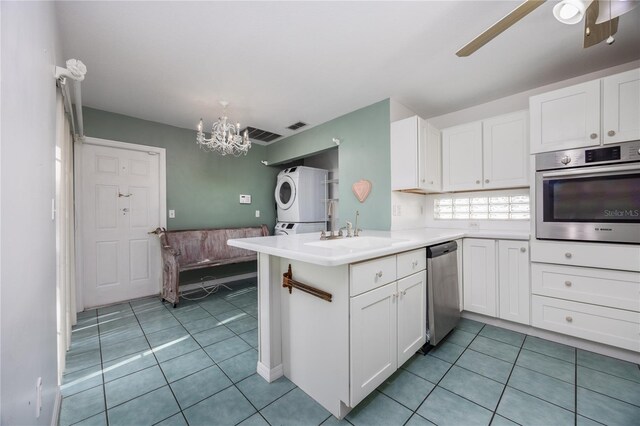 kitchen with appliances with stainless steel finishes, stacked washer / dryer, sink, white cabinets, and kitchen peninsula