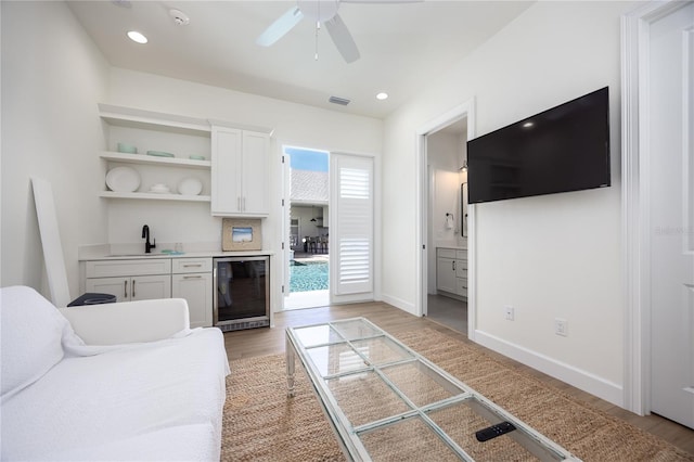 living room featuring light hardwood / wood-style floors, sink, ceiling fan, and wine cooler