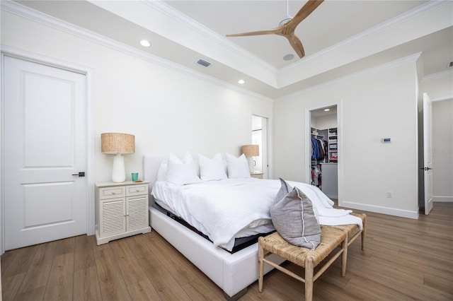 bedroom featuring ceiling fan, hardwood / wood-style floors, a walk in closet, a closet, and ornamental molding