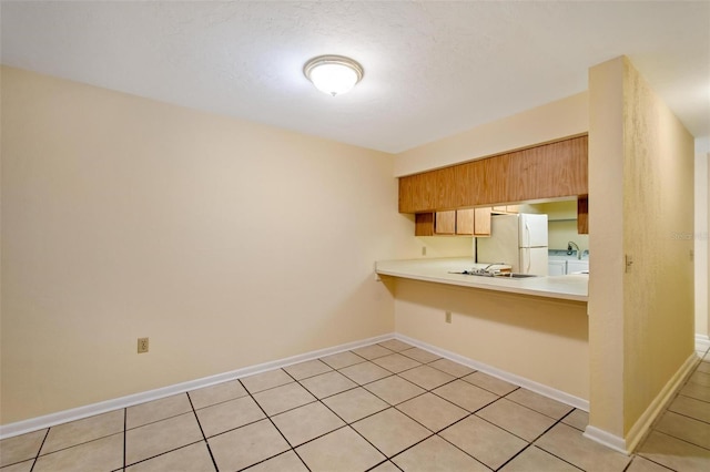 kitchen featuring light tile patterned floors, kitchen peninsula, and white fridge