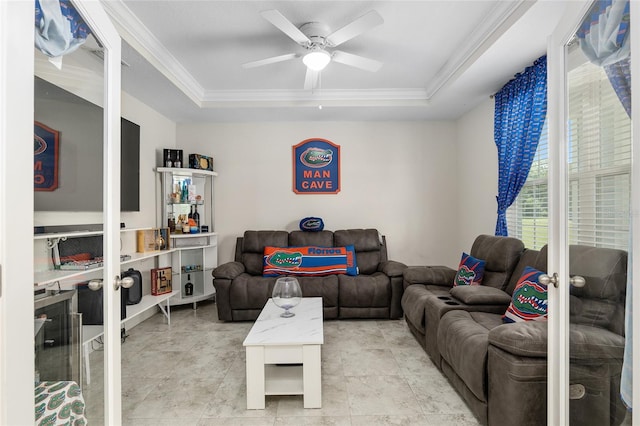 living room with ceiling fan, crown molding, a tray ceiling, and light tile patterned floors