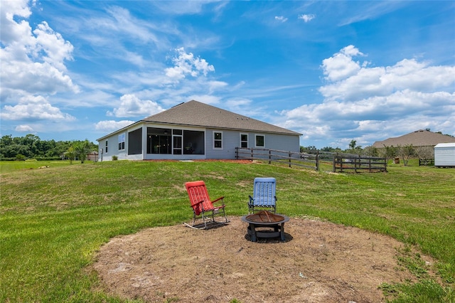 rear view of house with a sunroom, a yard, and a fire pit