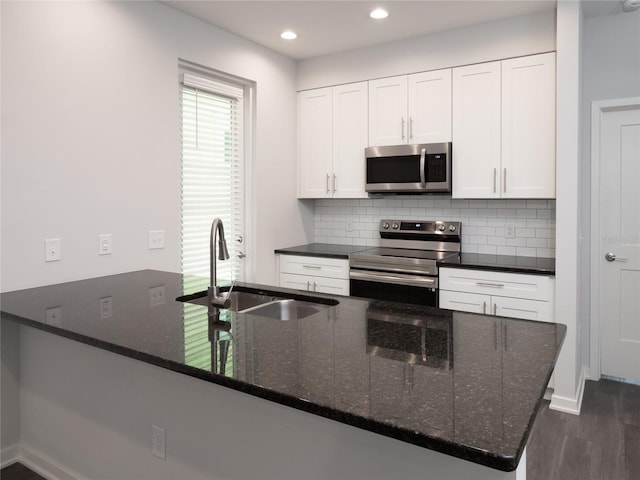 kitchen featuring dark hardwood / wood-style flooring, stainless steel appliances, white cabinetry, dark stone counters, and sink